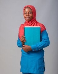An African Muslim lady, female student or businesswoman with head scarf called hijab holding a book...