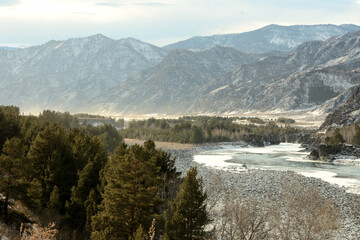 A clearing on the frozen bed of a beautiful river flowing through a winter valley surrounded by snow-capped mountains.