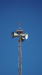 Mosque loudspeaker on top of the iron minaret. Blue sky background. Focus selected