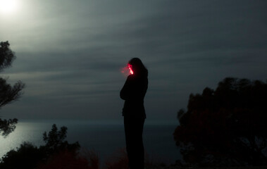 Woman silhouette holding red light at night