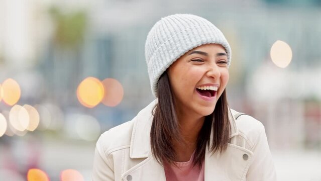 Winter portrait of laughing trendy girl with bokeh lights looking cheerful. Cute stylish and happy young woman smiling outside on a cold day in the city isolated against a blurred urban background