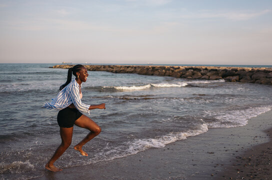 Young black woman running and laughing on the sea shore