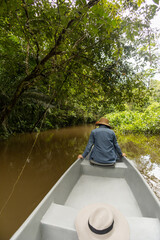 person from behind sitting on the tip of a canoe while walking along a river next to a jungle, nature and lifestyle of a traveler, tourism and means of transport