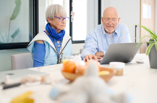Elderly Couple Using Laptop In Kitchen.