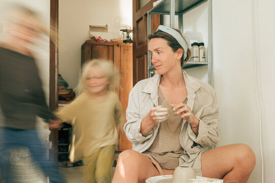 Children run near their mother while working on the potter's wheel