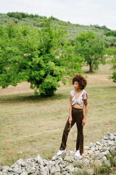 A pensive woman stands on a stone wall outdoors