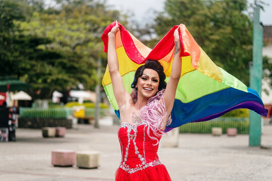 Drag queen raising the gay flag with both hands.