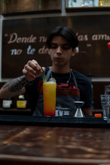 Bartender garnished a freshly brewed yellow drink with a green leaf. Waiter working at the bar with a drink for a client. Latino barman preparing a glass of juice