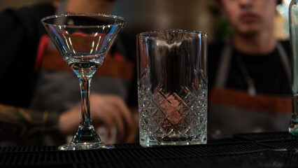 Close-up of a glass and a glass cup on the bar counter with the waiters in the background. Empty glasses for preparing drinks in the restaurant.
