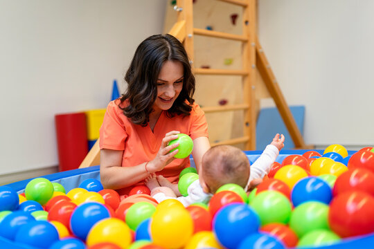 Happy Physiotherapist With Baby Playing In Ball Pit