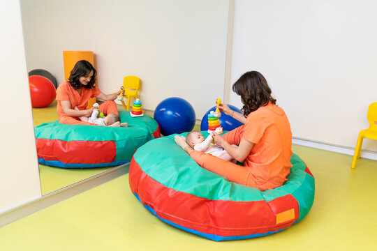 Content nurse showing toys to cute infant in playroom