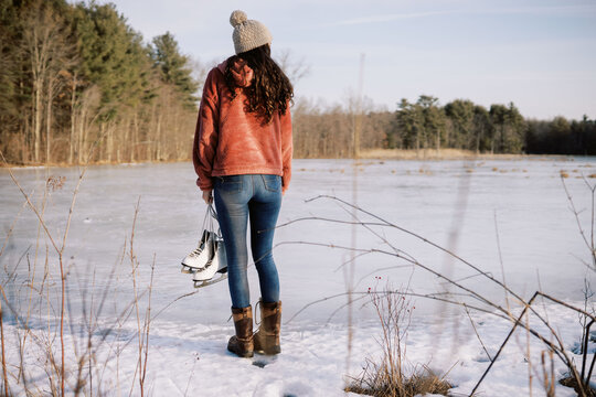young woman by lake holding skates