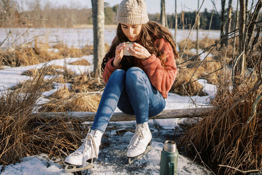 woman with ice skates blowing on a hot drink