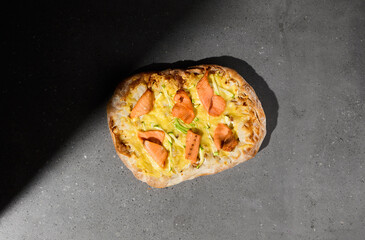 Italian pizza with salmon on dark background. Salmon pinsa on gray stone table with hard shadow. Roman pizza with smoked salmon on concrete background. Pinsa menu.