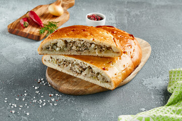 Classic pie with minced meat and potato on wooden board. Composition with meat pie on concrete background with textile and spices. Homemade pie with meat and potato in rustic style on gray table.
