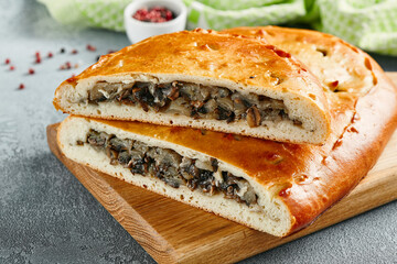 Classic pie with mushroom on wooden board. Composition with mushroom pie on concrete background with textile and spices. Homemade pie with mushrooms and onion in rustic style on gray table.