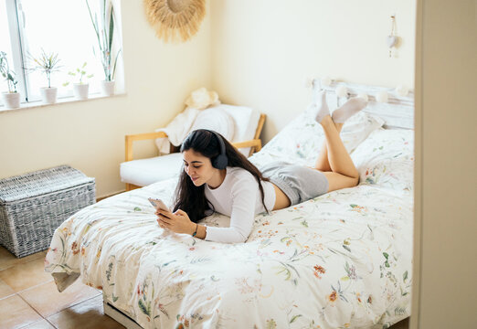 Woman listening music and using smartphone in bed