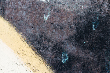 Texture of an old, metallic, black surface with scratches and rust. Remains of yellow, white and blue paint on the surface. Background, wallpaper. Close-up.