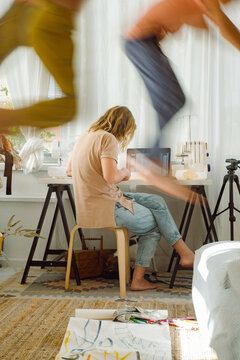 Two young boys jumps against the background of his mother in room