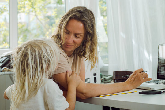 Little boy hugging his mom while working on a laptop