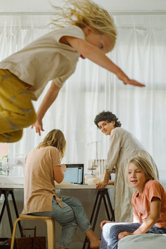 A young boy jumps against the background of his mother in room
