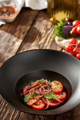 Traditional uzbek salad with tomatoes and sweet onion on black bowl. Tomatoes and onion salad on wooden background in rustic style. Appetizer from tomato and coriander.
