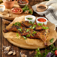 Traditional georgian dish - chicken tabaka on wooden background in rustic style. Roasted whole chicken in georgian style on wooden table. Chicken tabaka with sauces in rustic style.