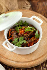 Beef ragout with vegetables in ceramic pot on wooden rustic background. Stew meat with coriander leaf on casserole in georgian style. Composition with meat ragout on wooden table with ingredients.