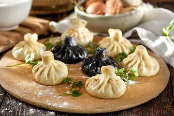 Composition of georgian khinkali on wooden table with coriander leaves. Georgian food - classic and black khinkali in rustic style. Traditional georgian dumplings khinkali on wooden background.