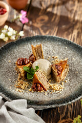 Traditional eastern sweets - baklava with walnuts and ice cream on wooden table. Turkish pastry baklava on modern plate in restaurant menu. Arabic dessert with nuts and honey on wooden background.