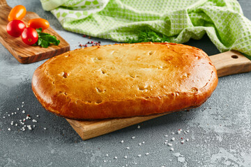 Classic pie with cabbage and eggs on wooden board. Composition with cabbage pie on concrete background with textile and spices. Homemade pie with cabbage in rustic style on gray table.