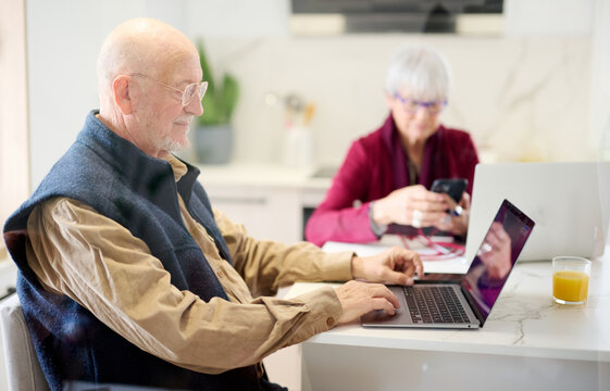 Pensioner using laptop in kitchen.