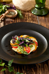 Traditional italian appetizer - caprese with slice tomatoes and mozzarella cheese. Caprese salad on wooden background in rustic style. Salad with red and yellow tomatoes and cheese on black plate.