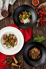 Composition with salads on wooden background with spices, textile and cherry tomatoes in rustic style. Set of salads: feta and eggplant; tomatoes and onion; meat and vegetables
