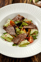 Steak salad with zucchini, tomatoes and lettuce on white plate. Fresh salad with roast beef and vegetables on wooden table in rustic style. Meat and vegetables salad on dark wooden background.