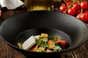 Salad with crispy eggplant, feta cheese and tomatoes on black plate. Fresh salad with eggplant and vegetables on wooden table in rustic style. aubergine and feta salad on dark wooden background.