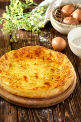 Traditional georgian pastry - megrelian khachapuri with cheese. Georgian cheese pie on wooden background in rustic style. Megrelian khachapuri with ingredients. Georgian cuisine.