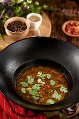 Georgian food - kharcho soup with coriander leaf in black plate on wooden table. Traditional georgian soup with lamb meat and spices in rustic style. Caucasian cuisine on dark wooden background.