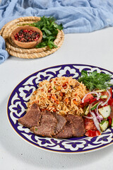 Traditional uzbek food - plov with beef. Eastern cuisine - pilaf with rice, meat and spices. Plov with beef on traditional uzbek plate. Composition of oriental ceramic plate with pilaf.