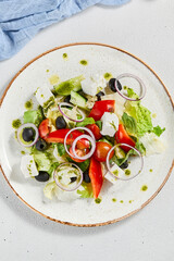 Classic greek salad with pesto sauce on ceramic plate. Vegetable salad with tomatoes, cucumber, paprika, onion and olives. Traditional grecian food. Greek salad on concrete background.