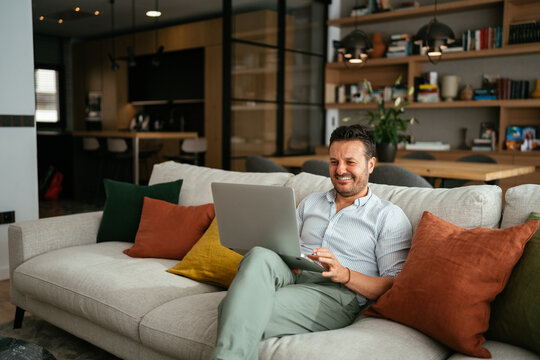 Cheerful freelancer using laptop on sofa