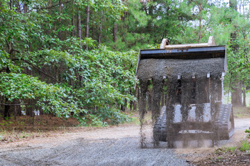There is a Bobcat loader tractor moving and unloading gravel on an old road reconstruction project