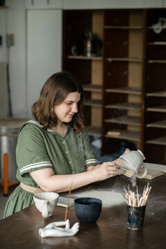 Young woman cleans a clay mug from excess clay dust