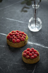 Two delicious raspberry tartlets with pistachios on a gray background