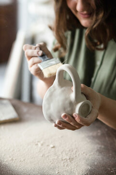 Young woman cleans a clay mug from excess clay dust