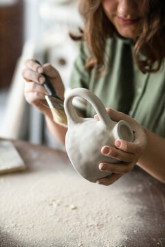 Young woman cleans a clay mug from excess clay dust