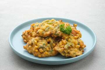 Perkedel Jagung or Bakwan Jagung, corn fritters is Indonesian traditional food. Savoury snack made of corn, egg, flour, spring onion, pepper and salt. Served in plate on grey background.
