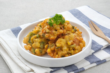 Perkedel Jagung or Bakwan Jagung, corn fritters is Indonesian traditional food. Savoury snack made of corn, egg, flour, spring onion, pepper and salt. Served in plate on grey background.
