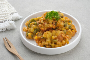 Perkedel Jagung or Bakwan Jagung, corn fritters is Indonesian traditional food. Savoury snack made of corn, egg, flour, spring onion, pepper and salt. Served in plate on grey background.
