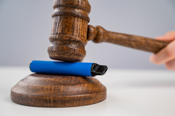 Judge hammering disposable vape with referee's gavel on white table. 